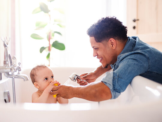 Junger Vater wäscht sein Baby in der Badewanne Bild: Vater wäscht Baby