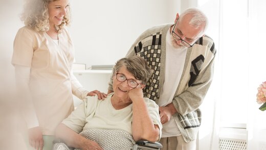 Senioren bei einem Pflegekurs kümmern sich um eine Dame im Rollstuhl