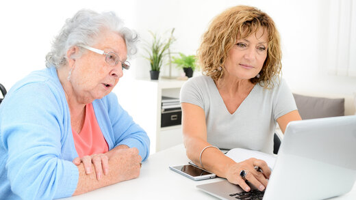 Eine jüngere Dame und eine Seniorin schauen gemeinsam in einen Computer