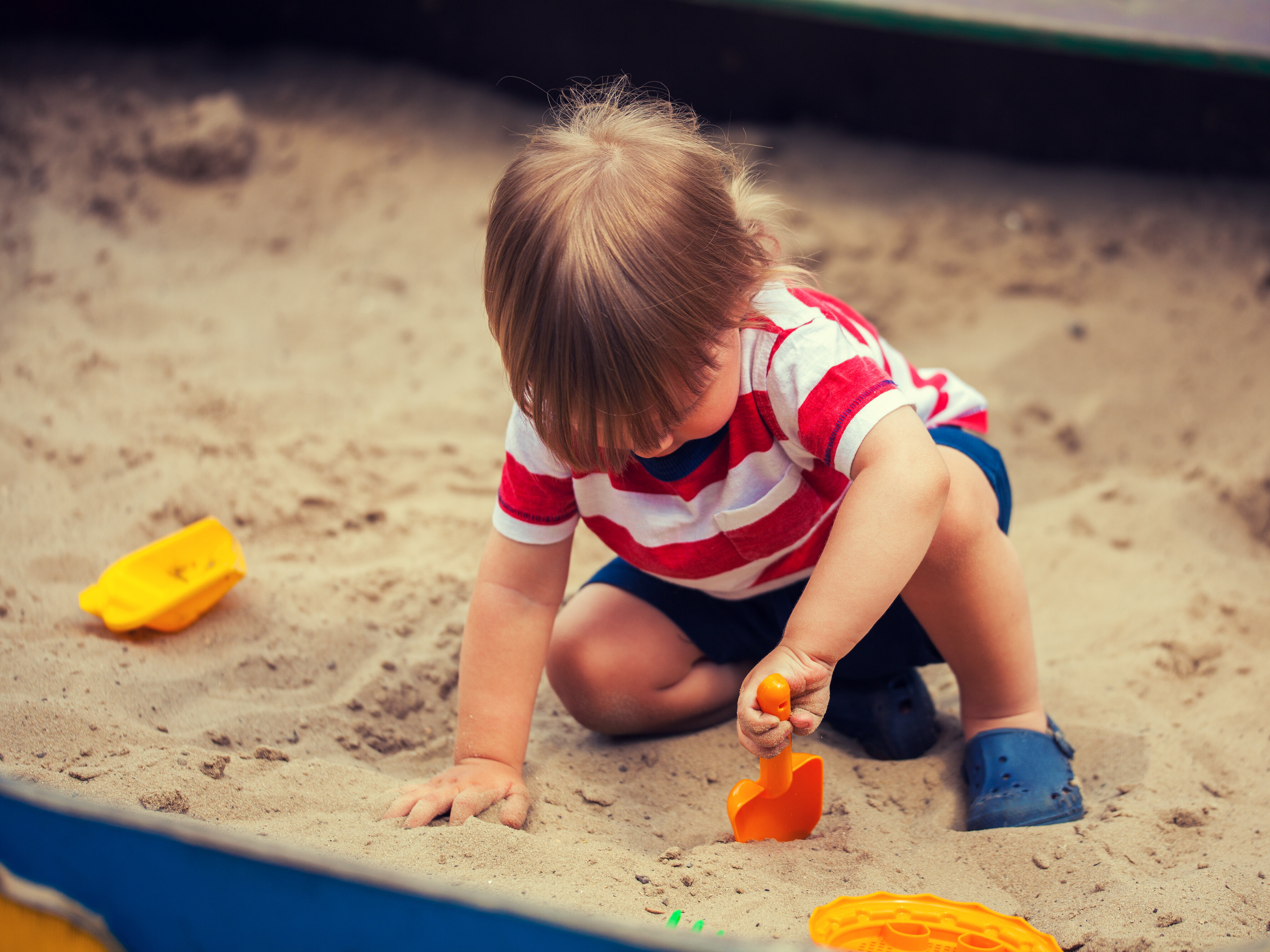 Kleinkind spielt im Sandkasten mit Förmchen