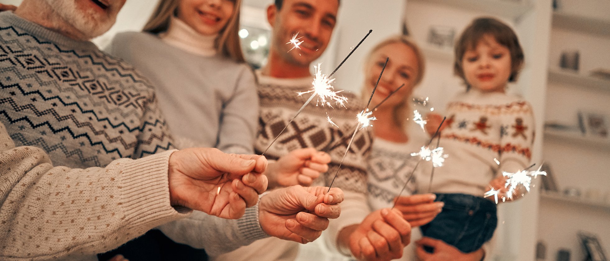 Eine Familie in weihnachtlichen Pullovern hält Wunderkerzen in die Höhe. Sie wirken alle fröhlich.