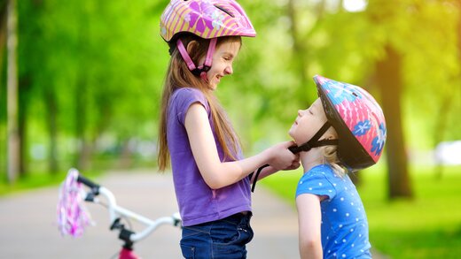 Mädchen setzt jüngerem Kind einen Fahrradhelm auf