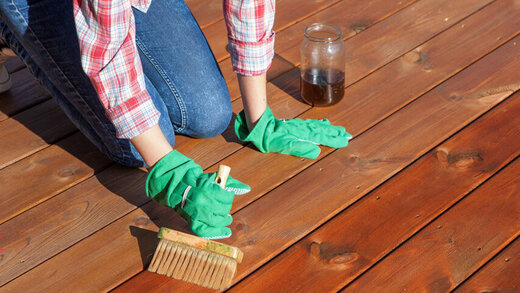 Eine Person streicht mit Handschuhen und einem Pinsel einen Holzboden