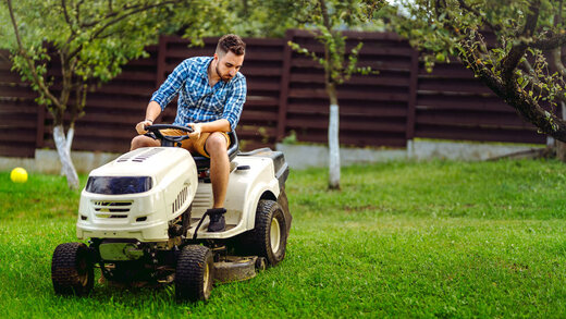 Ein Mann in Karohemd sitzt auf einem weißen Aufsitzrasenmäher und fährt durch seinen Garten.