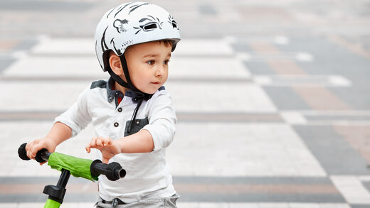 Kleines Kind sitzt mit dem Helm auf einem Laufrad