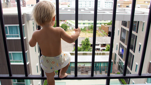 Kleinkind steht an Fenster mit Fensterschutzgitter