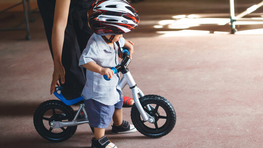 Mutter hilft einem kleinen Kind beim Laufradfahren mit Helm