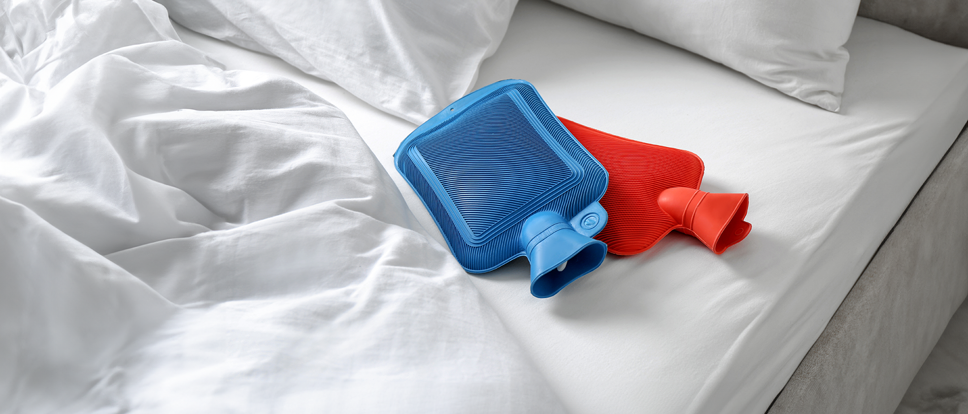 Zwei bunte Wärmflaschen liegen im Bett. 