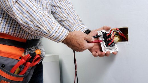 Ein Handwerker prüft mit Geräten den Strom an einer elektrischen Leitung. Die Situation wirkt potenziell gefährlich.