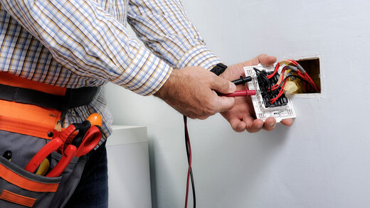 Ein Handwerker prüft mit Geräten den Strom an einer elektrischen Leitung. Die Situation wirkt potenziell gefährlich.