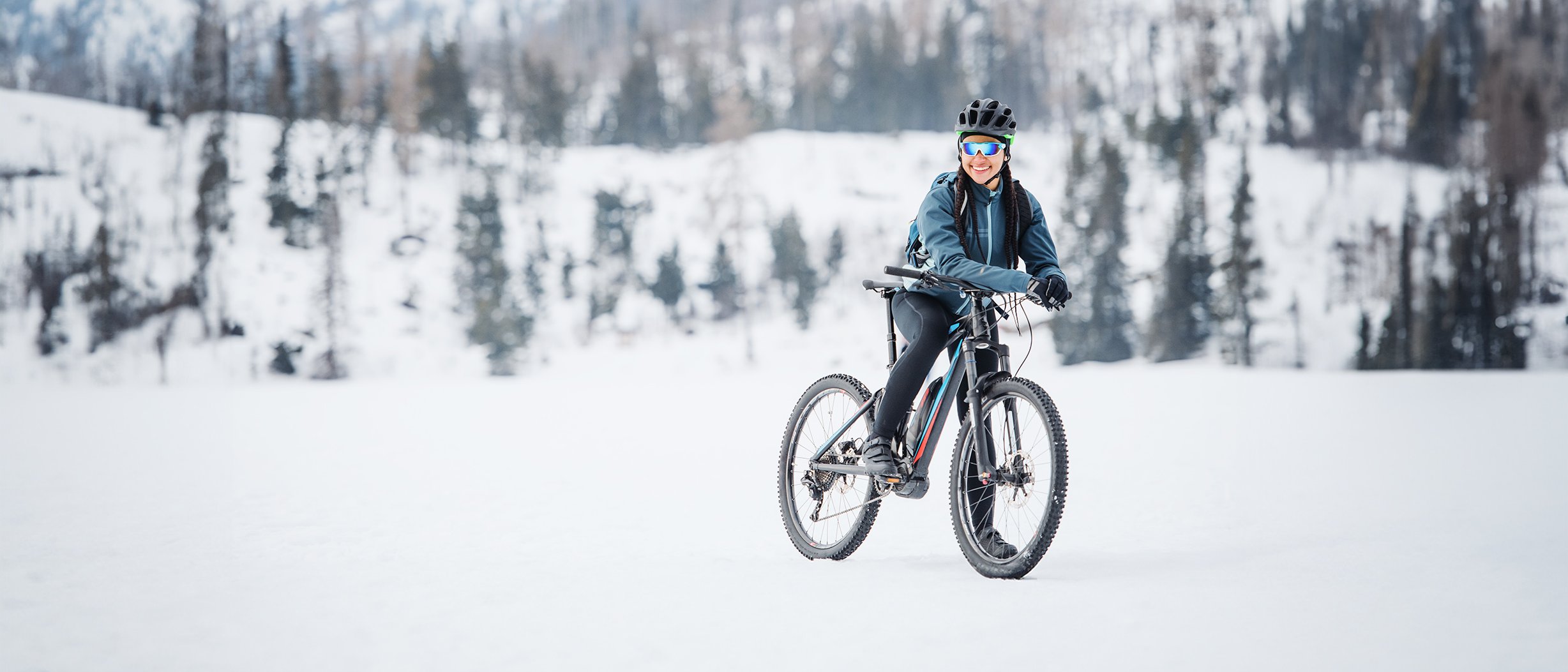 Eine Frau in sportlicher Kleidung sitzt auf einem Rad. Die Landschaft ist winterlich und alles ist mit Schnee bedeckt. 