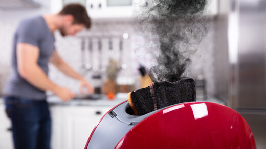 Verbrannter Toast mit Rauch und Mann im Hintergrund in der Küche