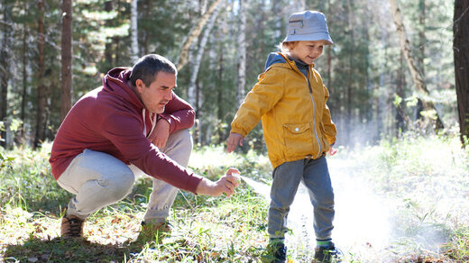 Ein Vater sprüht sein Kind im Wald mit Insektenschutzmittel ein