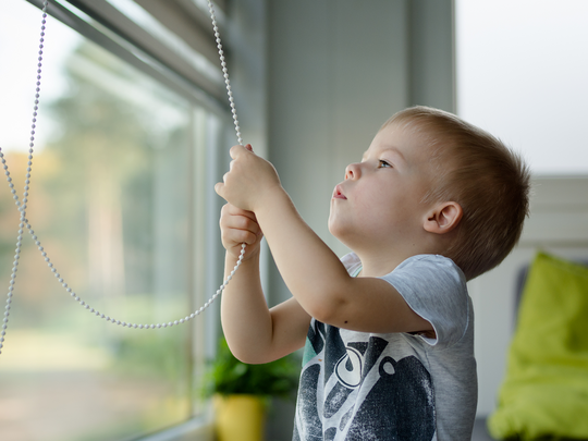 Ein Junge zieht an der Zugkette eines Rollos am Fenster.