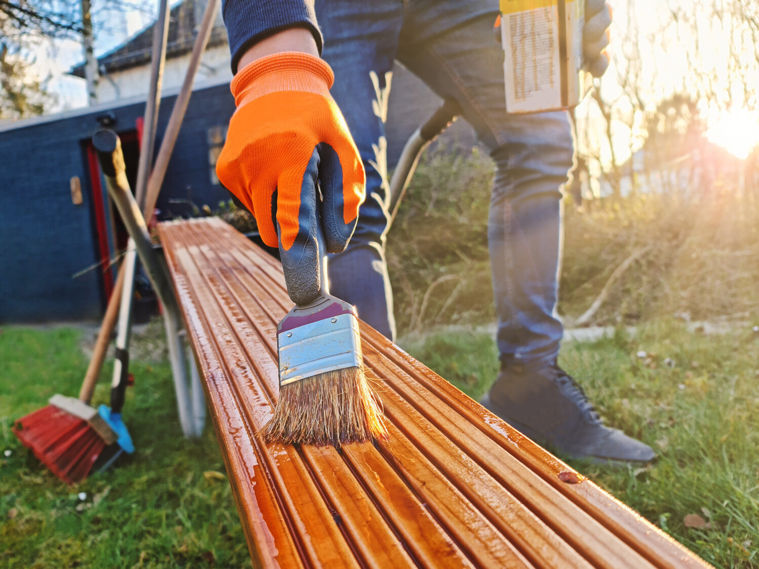 Jemand pinselt Leinöl auf ein Stück Holz. Die Person befindet sich in einem Garten. 