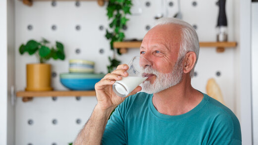 Ein Senior steht in seiner Küche und trinkt ein Glas Milch.