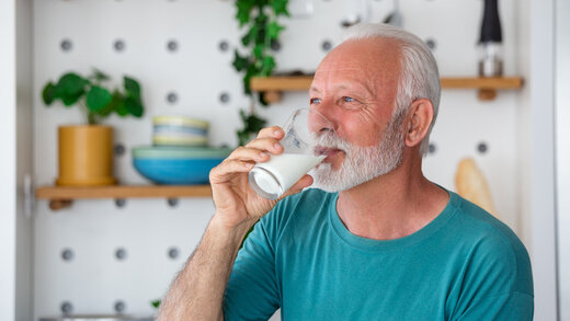 Ein Senior steht in seiner Küche und trinkt ein Glas Milch.