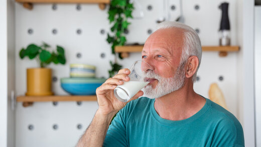 Ein Senior steht in seiner Küche und trinkt ein Glas Milch.