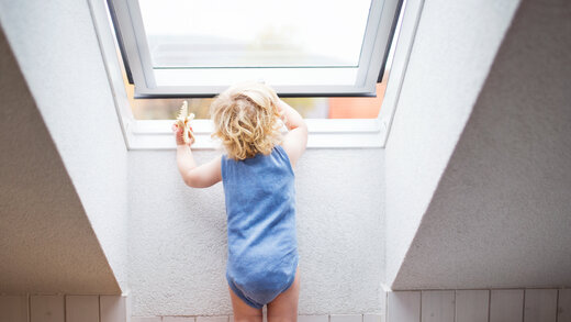 Kleines Kind steht an einem Dachschrägen-Fenstr