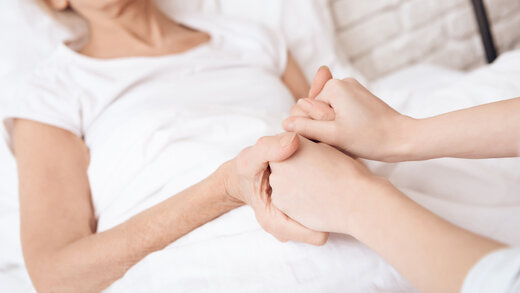Zwei Hände helfen einer Person im Bett beim Aufstehen
