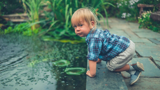 Kleiner Junge beugt sich über den Rand eines Teiches