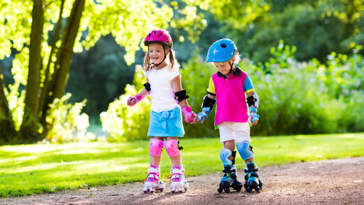 Zwei Kinder fahren mit Helm und Schutzausrüstung Inliner und Rollschuhe