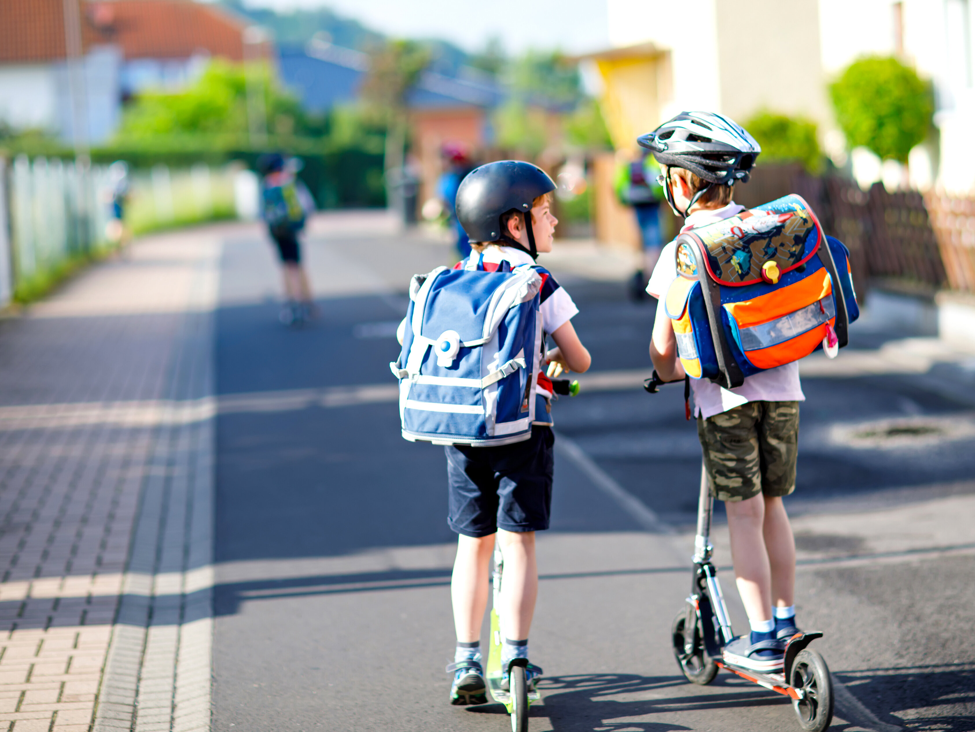 Zwei Kinder fahren mit Tretrollern zur Schule