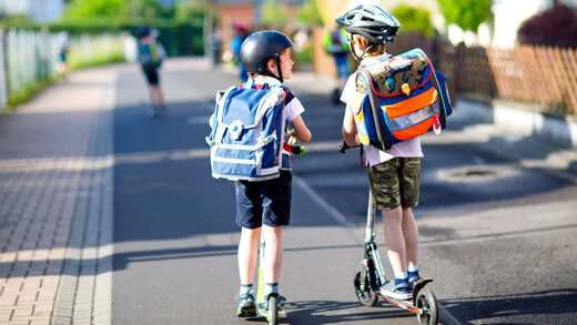 Zwei Kinder mit dem Roller auf dem Weg zur Schule