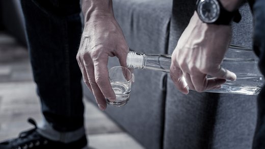 Ein Mann schenkt sich Alkohol ein; die Szene steht im Kontext von Alkoholsucht bei Pflegenden.