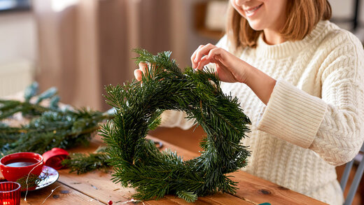 Junge Frau bastelt einen Adventskranz. Dabei werden brennbare Materialien wie Tannenzweige und Kerzen verwendet, was eine potenzielle Brandgefahr darstellen kann.