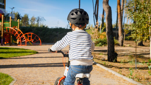 Kind mit Laufrad und Fahrradhelm auf dem Weg zum Spielplatz