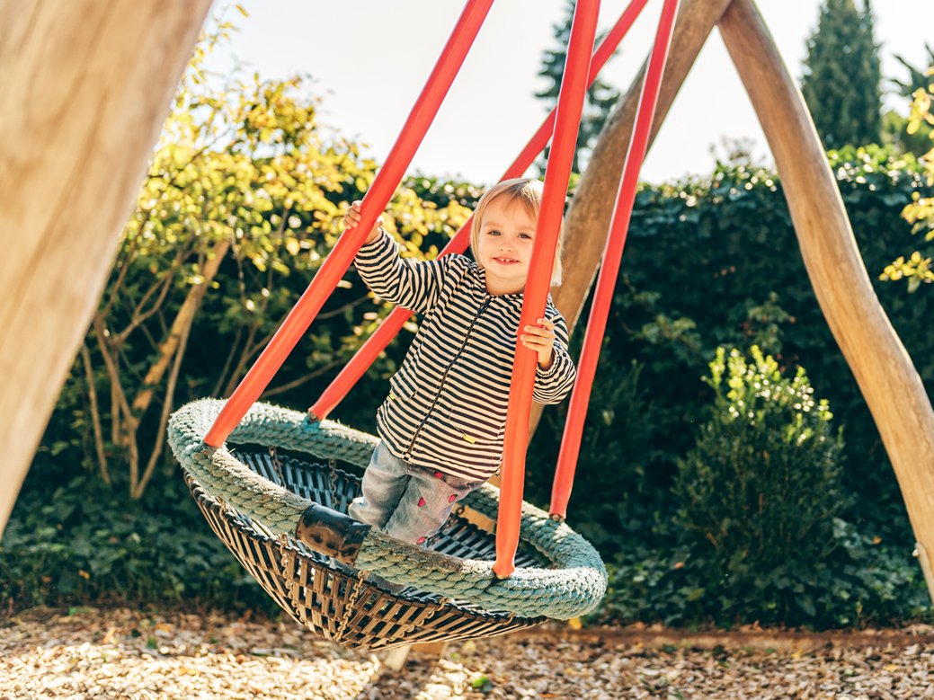 Kleinkind auf einer sicheren Nestschaukel auf dem Spielplatz