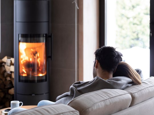 Ein Paar sitzt auf dem Sofa vor einem Kamin, in dem ein Feuer brennt. 
