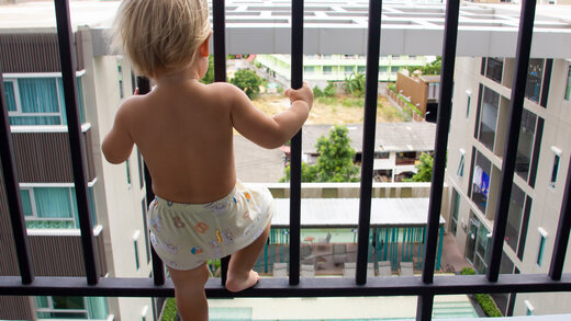 Ein kleines Kind steht an einem Balkon mit Fallschutz-Gitter