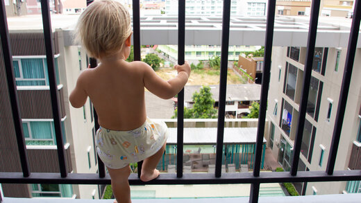 Kleines Kind steht auf einem Balkon mit Gitterstäben zum Schutz vor Sturz