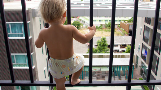 Kleines Kind steht auf dem mit Gitterstäben gesicherten Balkon