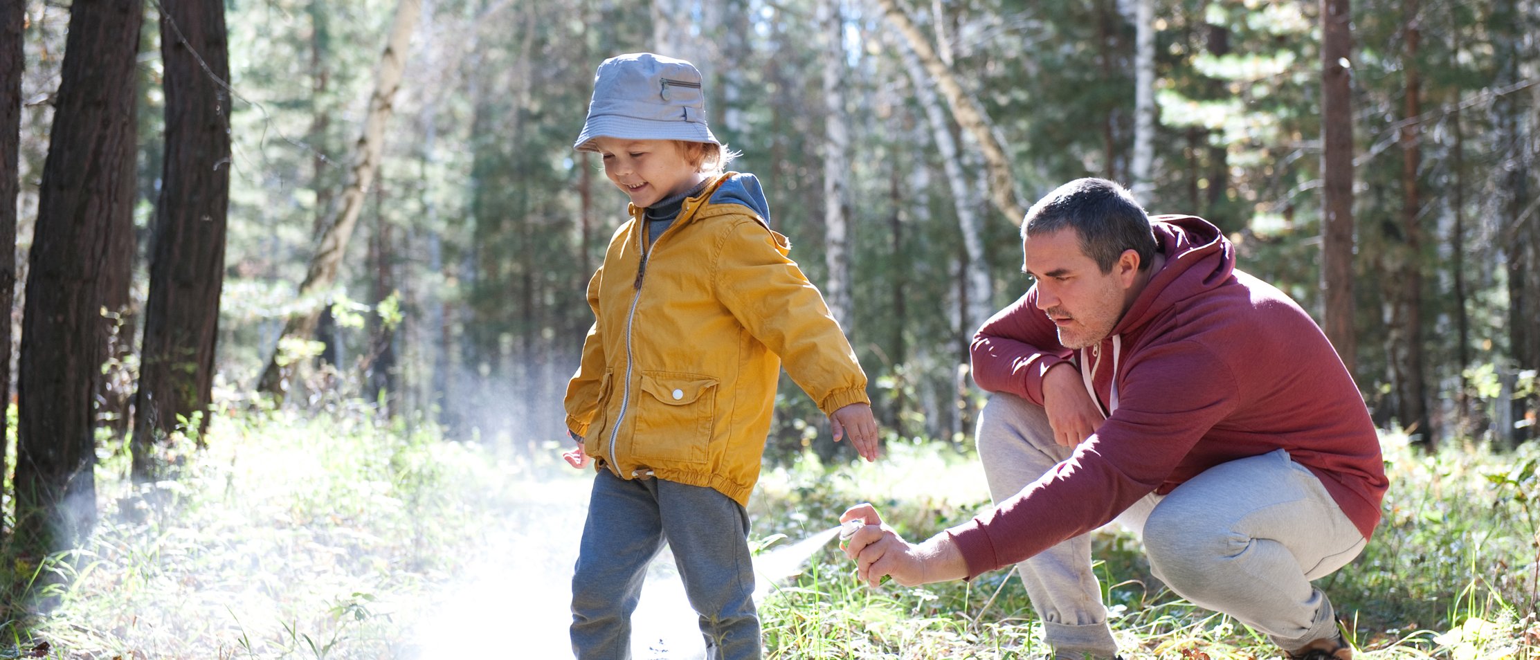 Vater sprüht Kleinkind mit Zeckenschutzspray ein