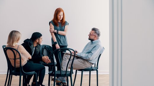 Mehrere Personen sitzen in einem Kreis und sprechen miteinander; die Szene zeigt eine Selbsthilfegruppe für pflegende Angehörige.
